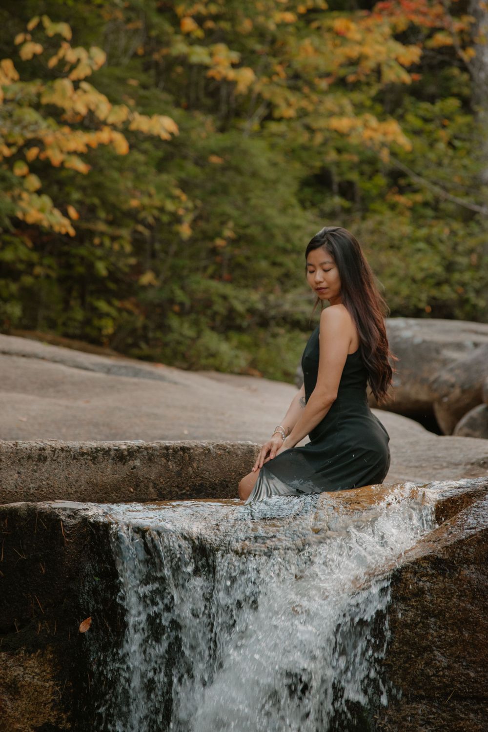 A waterfall cascades over rocky ledges surrounded by autumn foliage in a scenic forest setting. Diana's Bath's, New Hampshire