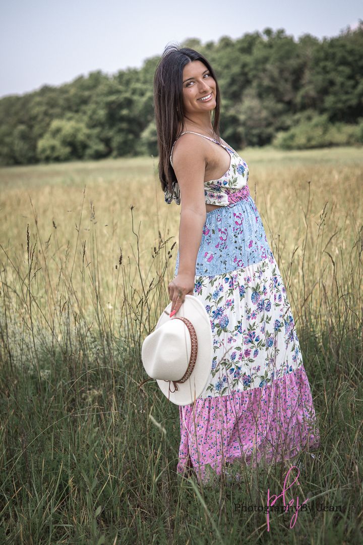 Summer portrait in a field showing a floral tiered maxi dress and white straw hat against a natural meadow background.
