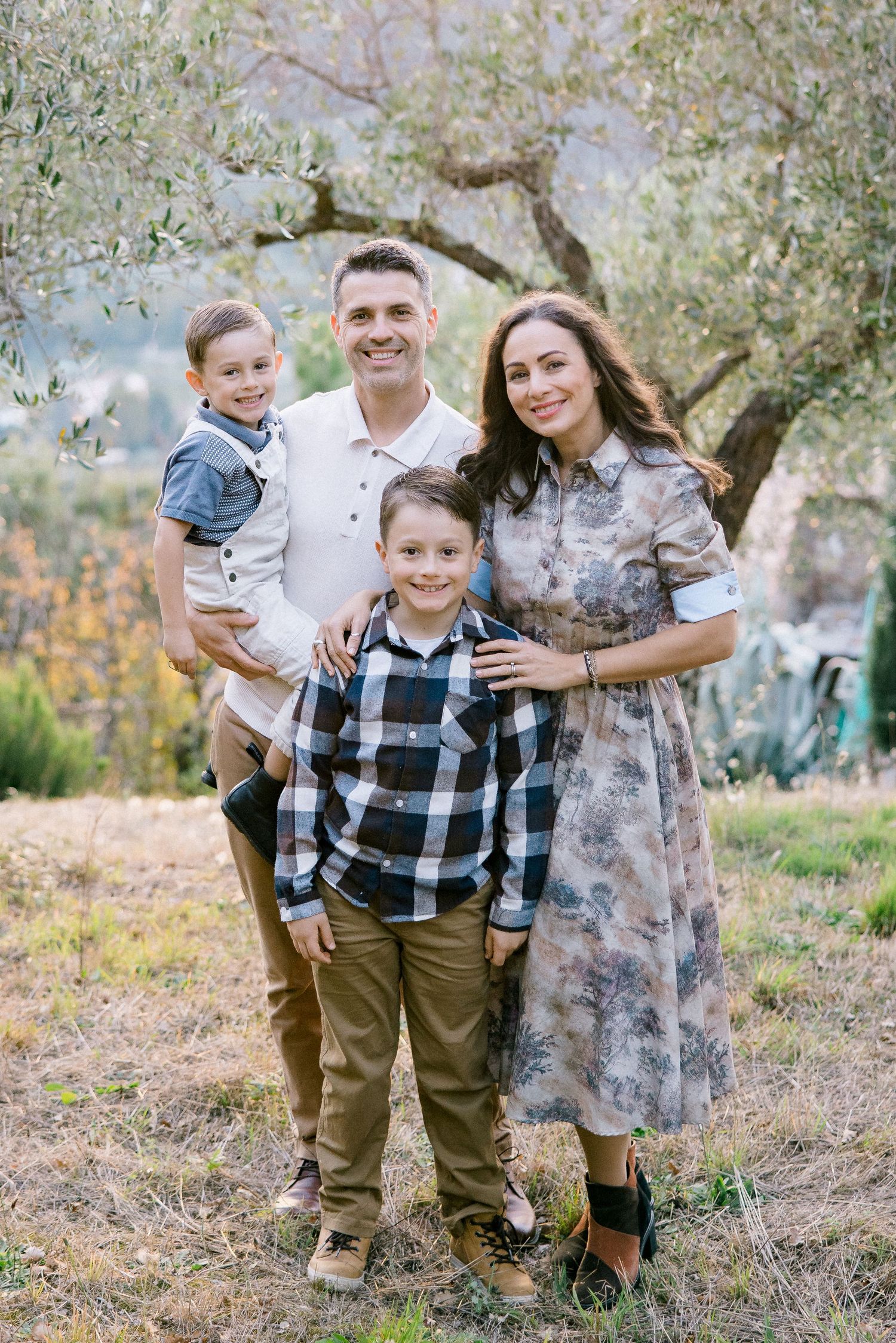 A father, mother and two children are standing next to each other and smiling. The smallest child is being held by the father.