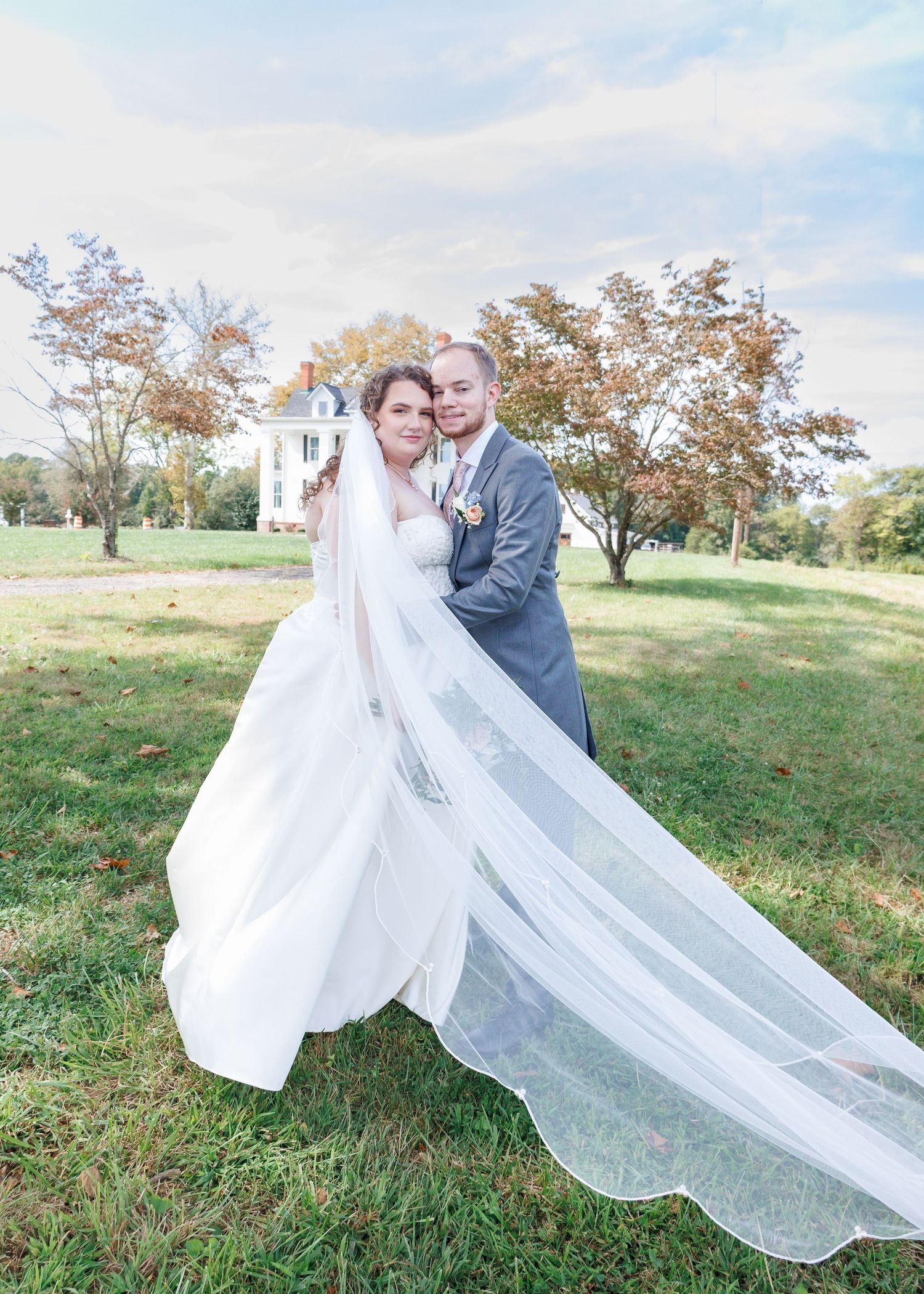 Wedding couple poses outdoors with flowing veil in autumn landscape.