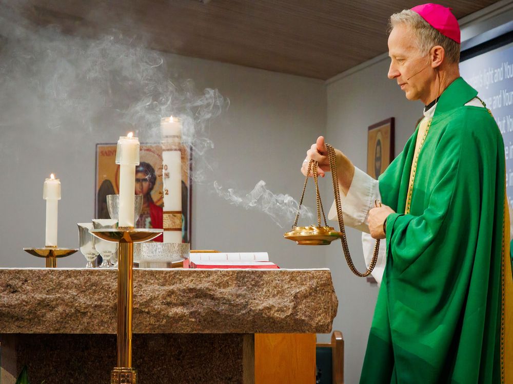 A religious service with incense being used at an altar by a priest wearing green vestments in a church setting.