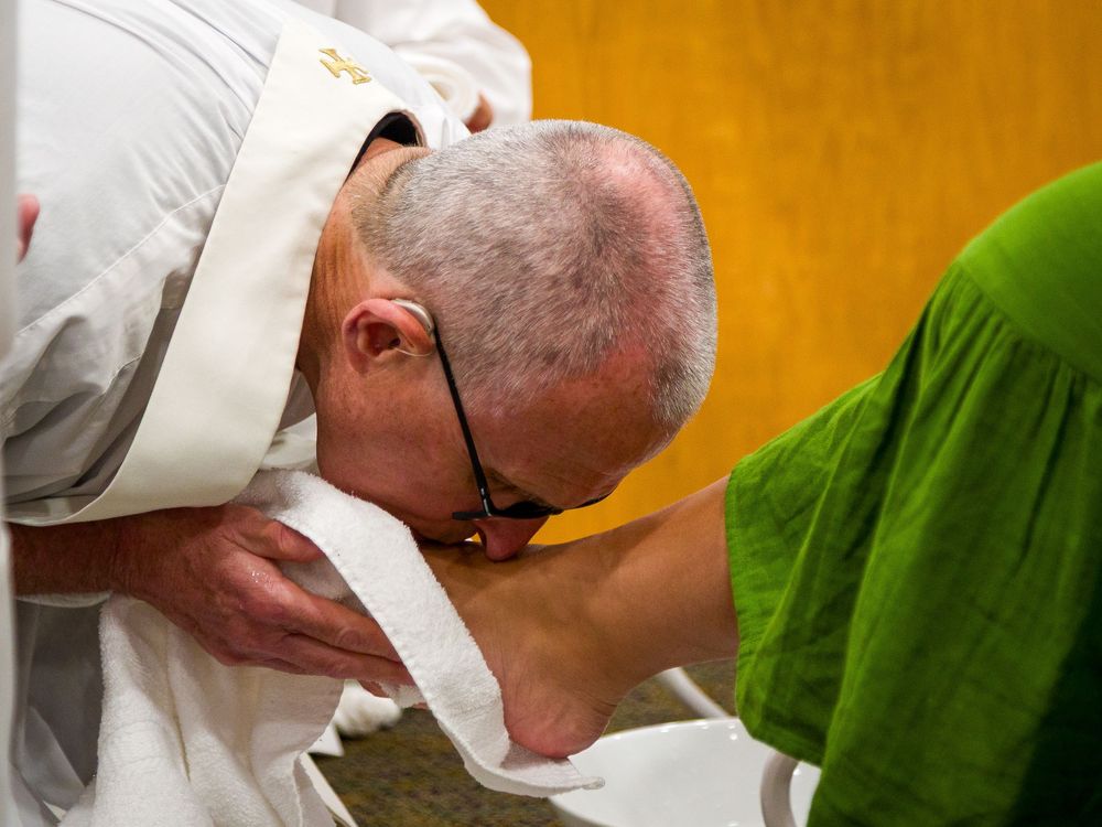 A religious leader bows down to kiss someone's foot in a ceremonial setting.