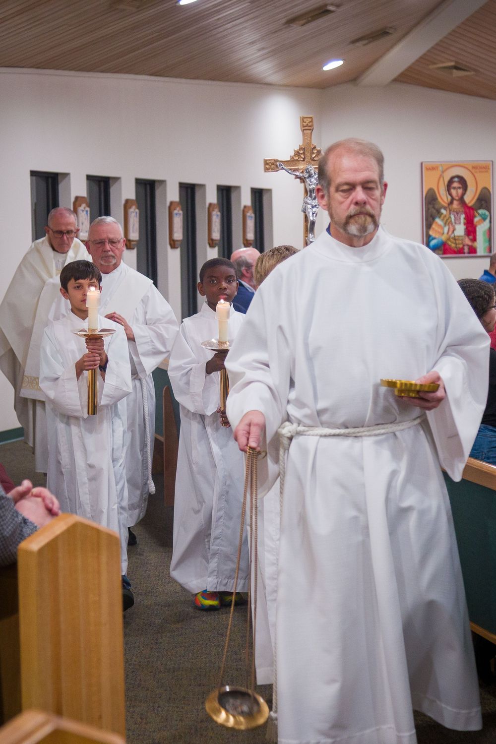 Religious ceremony with clergy members in white robes holding candles and staffs during a church service.