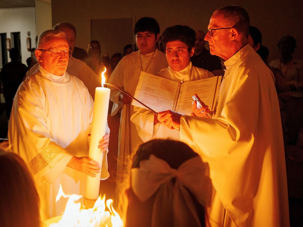 Religious clergy conduct a candlelit Easter Vigil service while reading from liturgical books in white robes.
