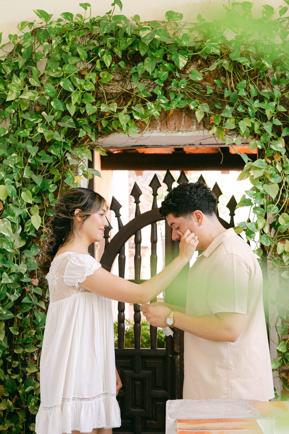 A tender moment between two people under an ivy-covered archway with a decorative gate.