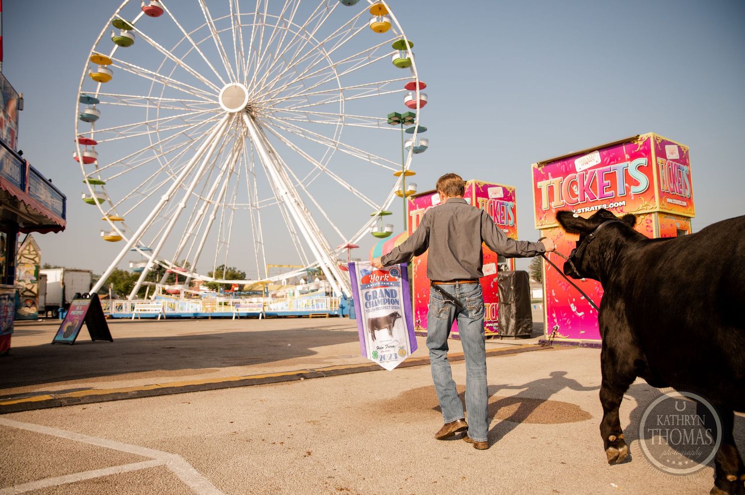 A black show animal walks with its handler near a large ferris wheel and ticket booth.