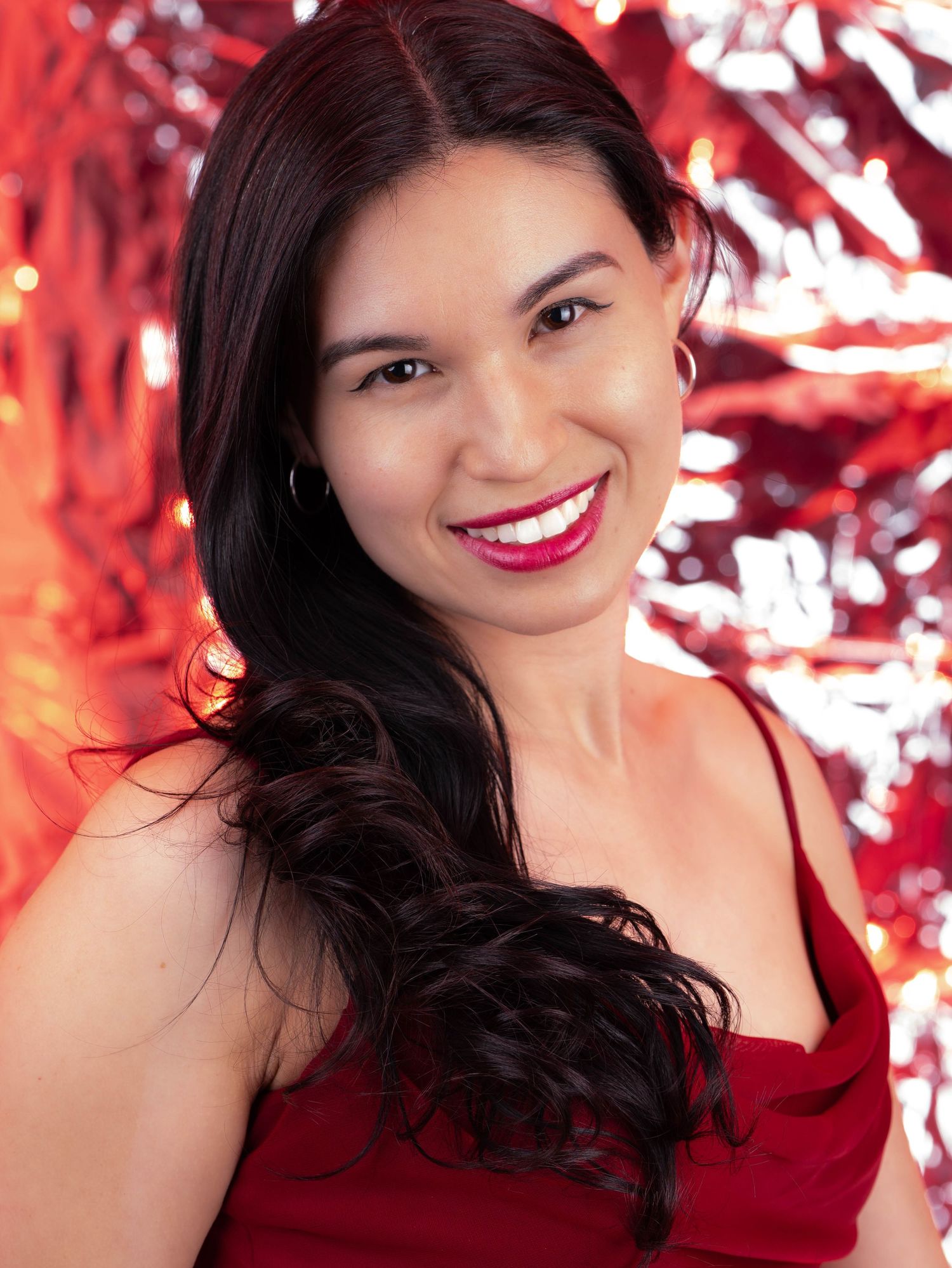 Portrait against red metallic backdrop wearing red evening dress with long dark hair.
