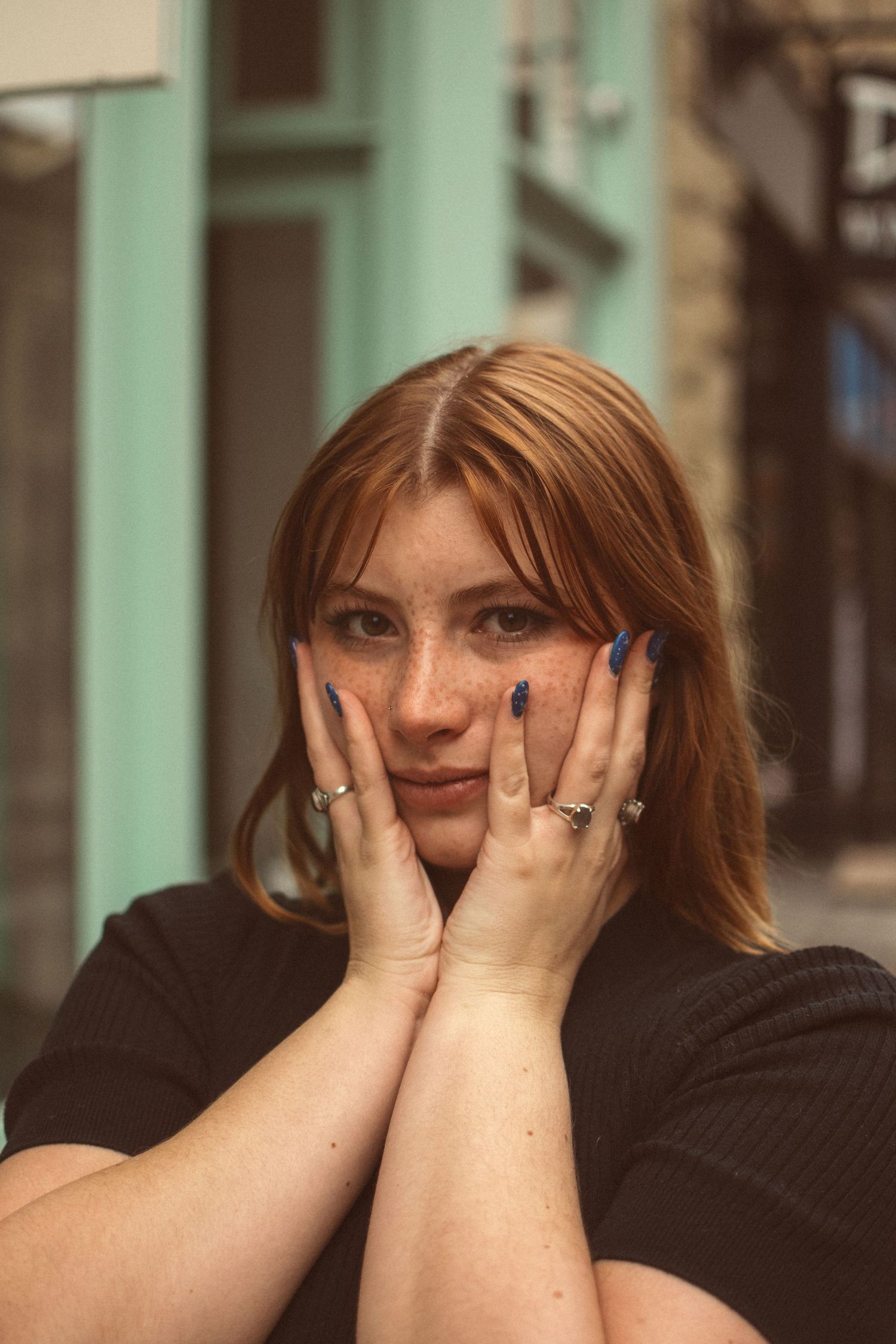 A person with rings on their fingers frames their face with their hands while looking at the camera.