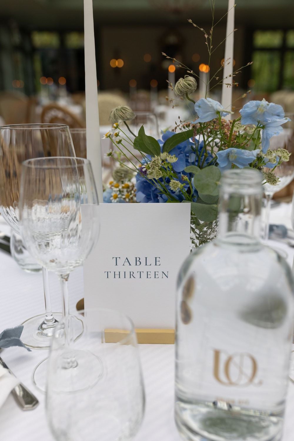 A wedding table detail with Table Thirteen card, blue flowers, and glassware.