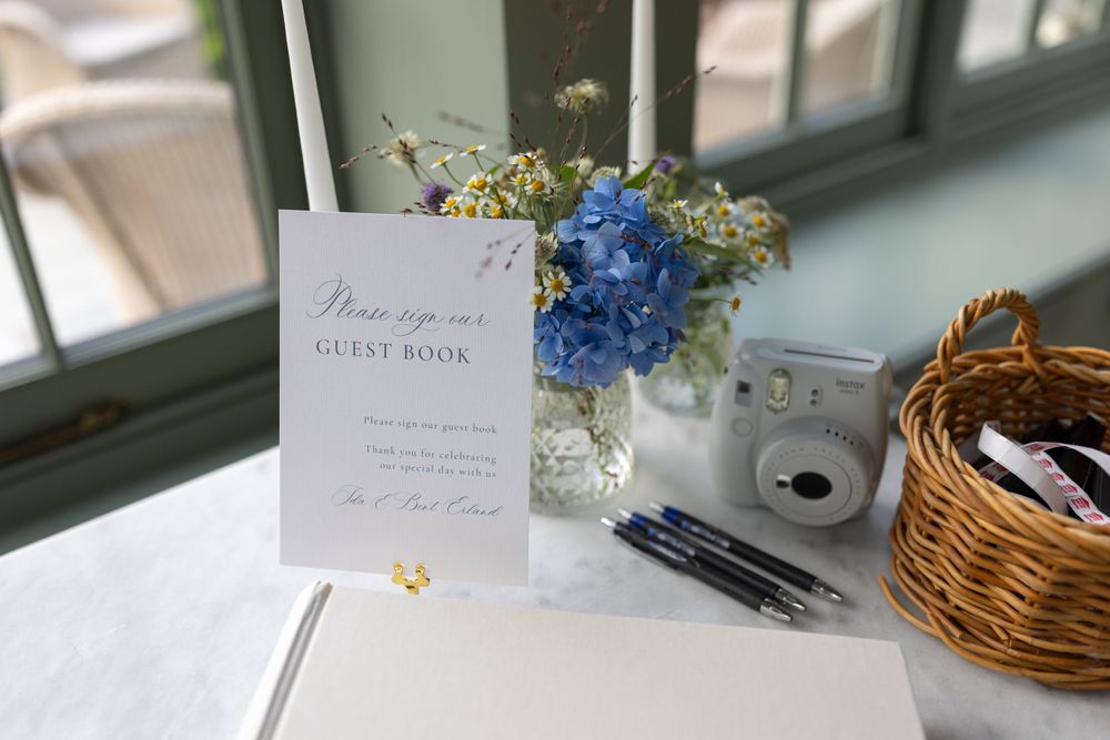 A wedding guest book station with blue hydrangea flowers and an instant camera.