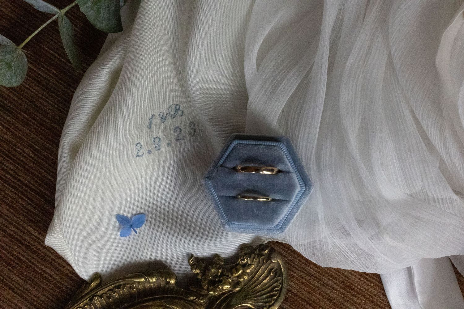 Wedding ring box and dress details with blue butterfly decorations on wooden surface.