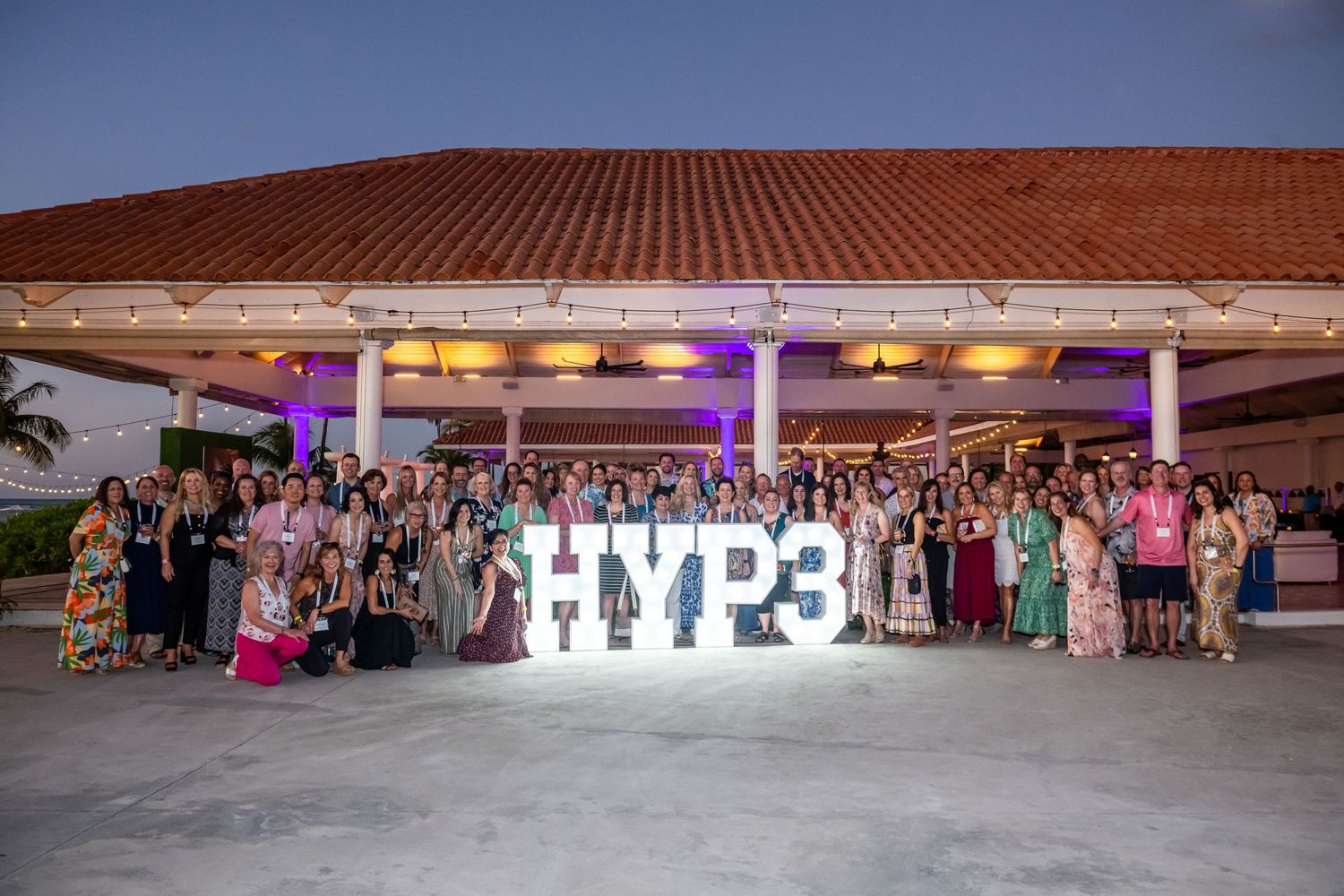 A large group celebration with illuminated HYPE letters and purple lighting at an outdoor venue.