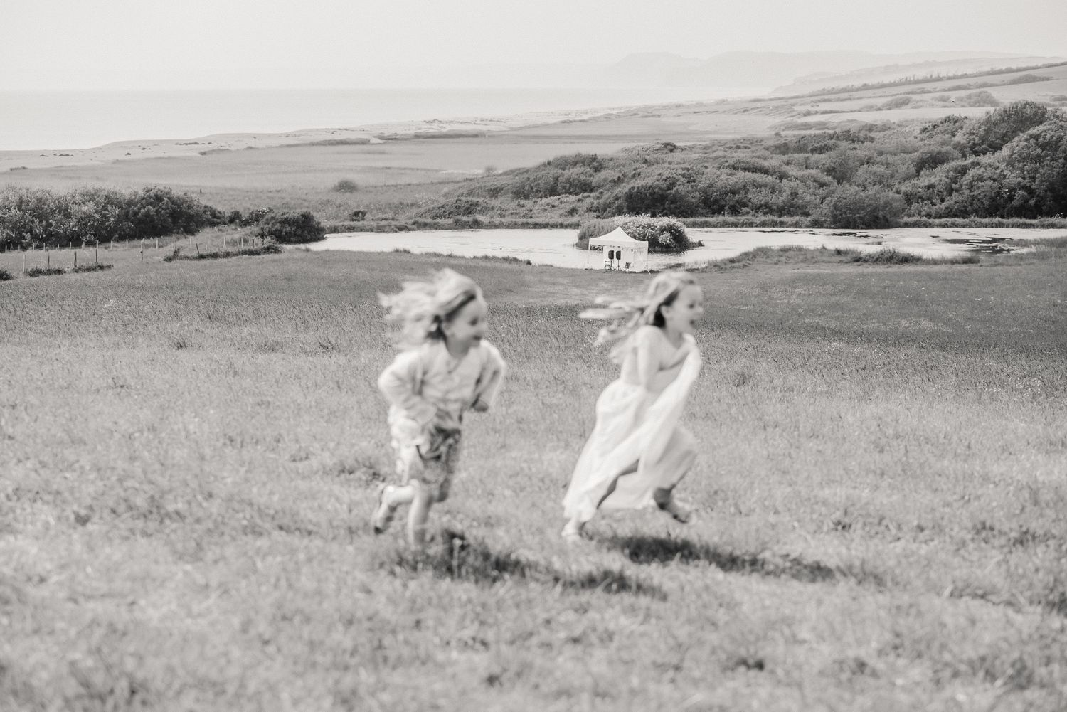 Children playing at wedding overlooking chesil beach. Celebrant wedding Dorset. Dorset wedding. Outdoor wedding. Taddle Farm tent. Bridport