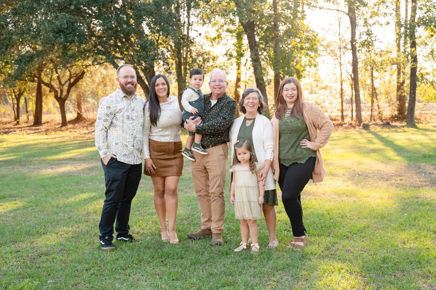 A family of five holding hands while walking through a sunlit park at sunset.