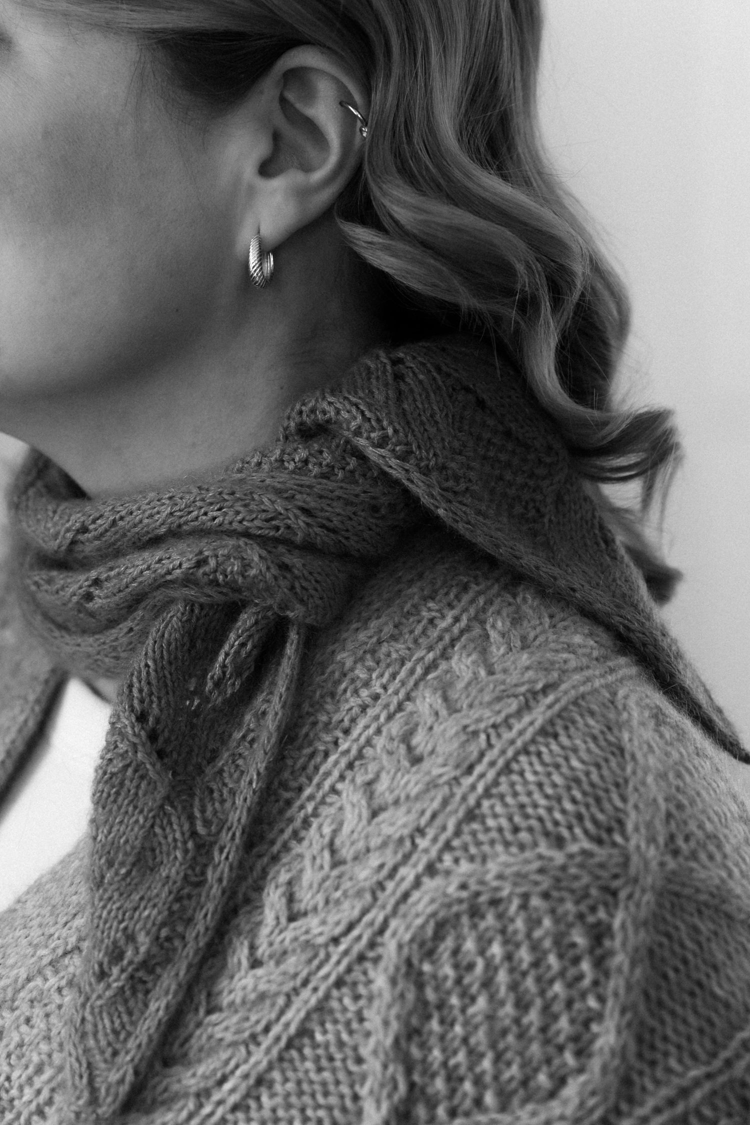 Close-up black and white image showing wavy hair and a textured knit sweater with cable patterns.