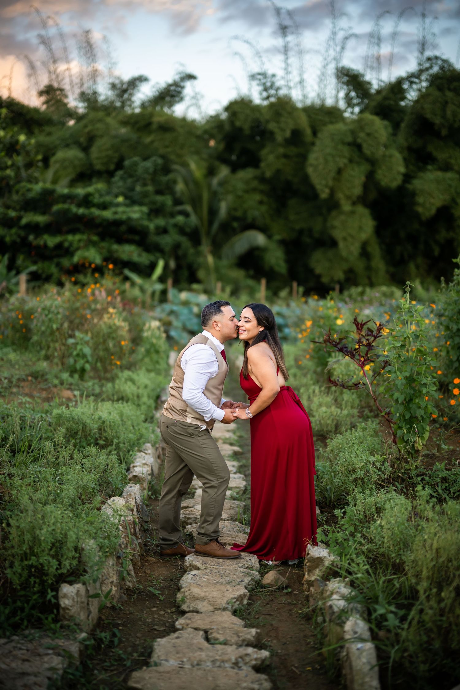 A couple shares an intimate moment on a stone path in a lush garden at sunset.