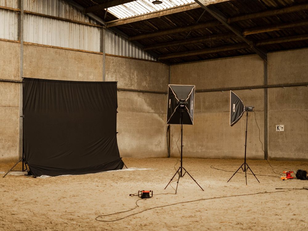 Photography studio setup with black backdrop and professional lighting in indoor horse arena.