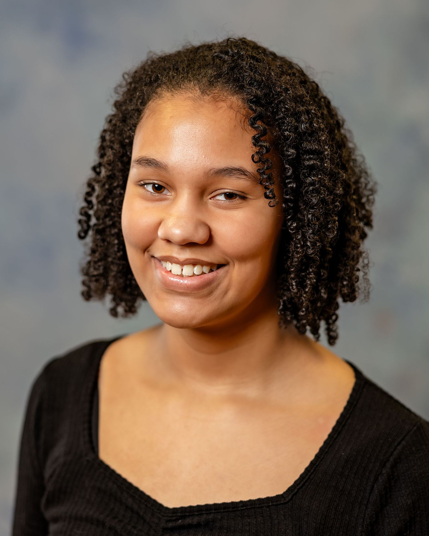 Smiling young woman with natural curly hair wearing black top poses for portrait photo.