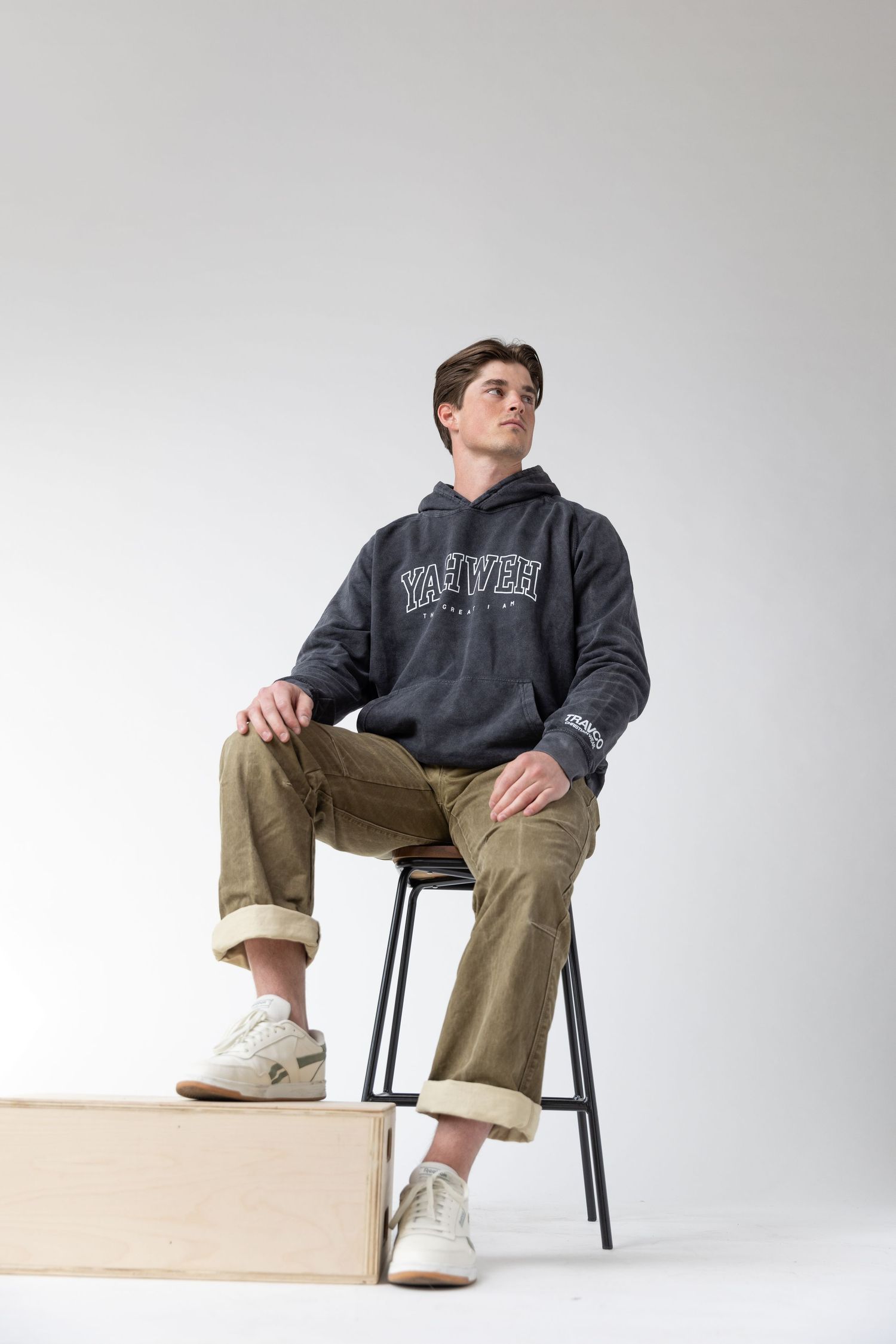 Group wearing casual hoodies and sweaters pose against white background while sitting on black chairs.