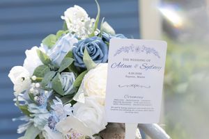 Wedding ceremony program card displayed with a bouquet of blue and white roses for Adam and Sydney.