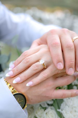Close-up of newlyweds hands showing diamond engagement ring and wedding band with gold watch detail.