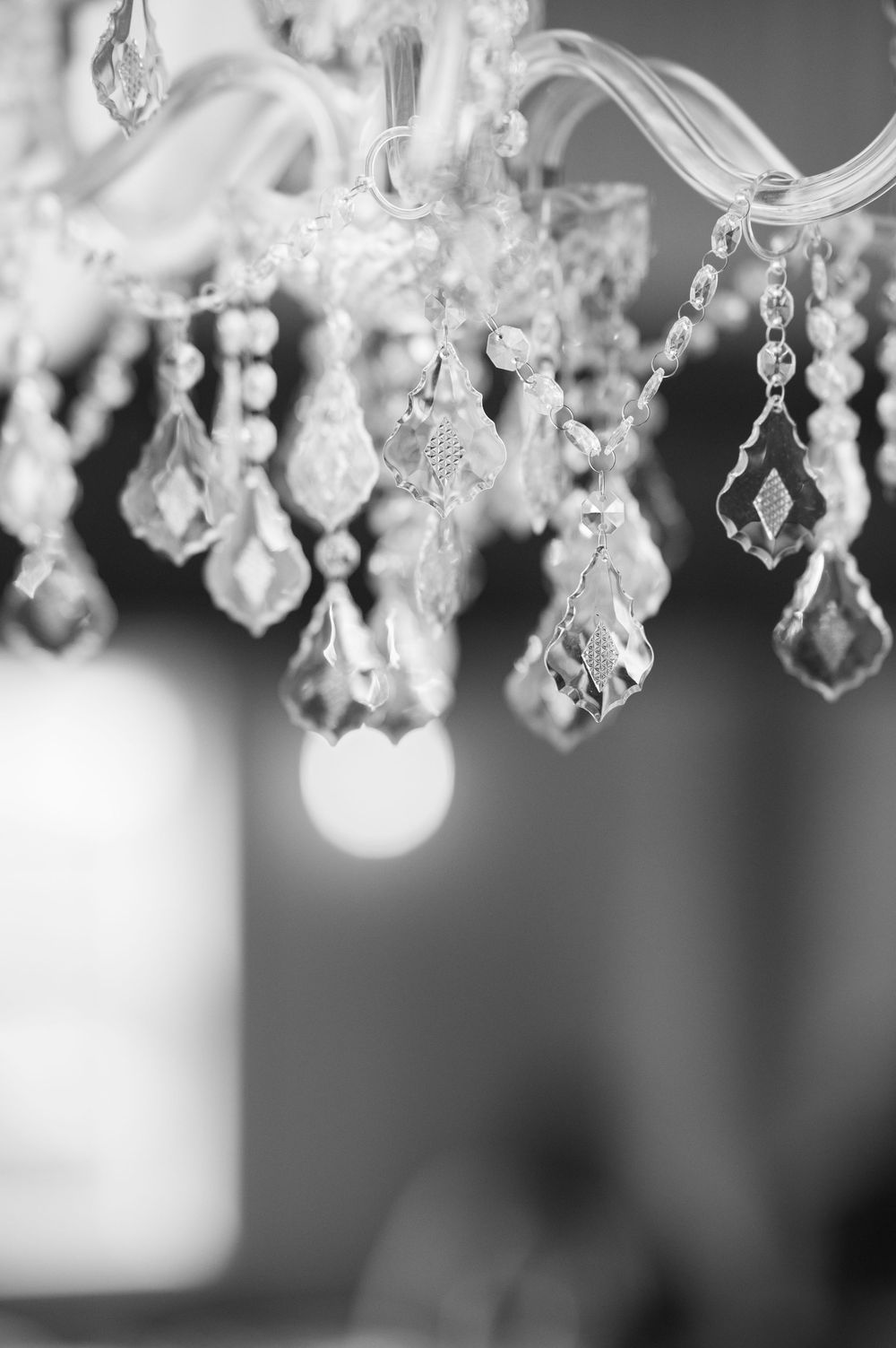 Elegant crystal chandelier with hanging glass pendants photographed in black and white at a wedding venue.