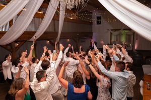 Wedding guests celebrating on the dance floor with hands raised in a festively decorated barn venue.