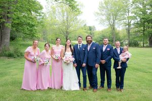 Wedding party posing outdoors with bridesmaids in pink dresses and groomsmen in navy blue suits on green grass.