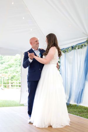Bride and older gentleman sharing a father-daughter dance under a white tent with blue drapery decor.