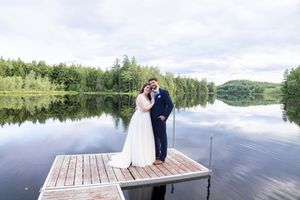 Bride and groom posing together on a wooden dock with a stunning mirror-like lake and green forest backdrop.