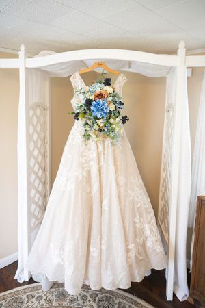 Lace ballgown wedding dress hanging with a blue and white floral bouquet in a bridal suite.