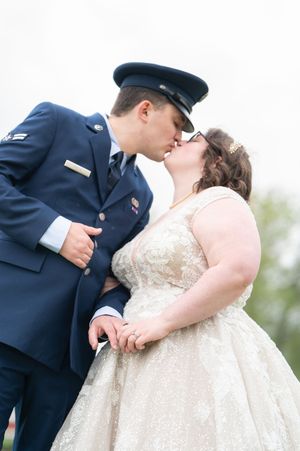 Military groom in Air Force dress uniform kissing bride in sparkly ball gown outdoors on wedding day.