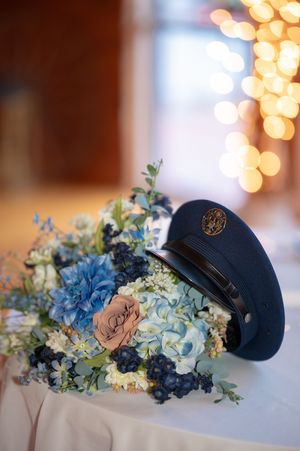 Military dress cap resting on a blue hydrangea and white floral wedding centerpiece with bokeh lights.