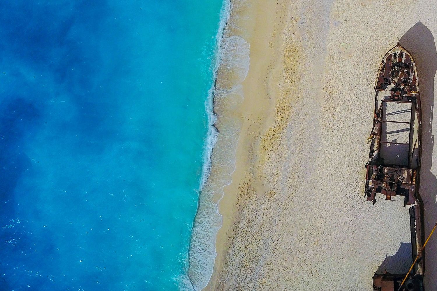 Zakynthos Greece drone photography of the Navagio shipwreck on the sandy beach next to vibrant turquoise ocean water.
