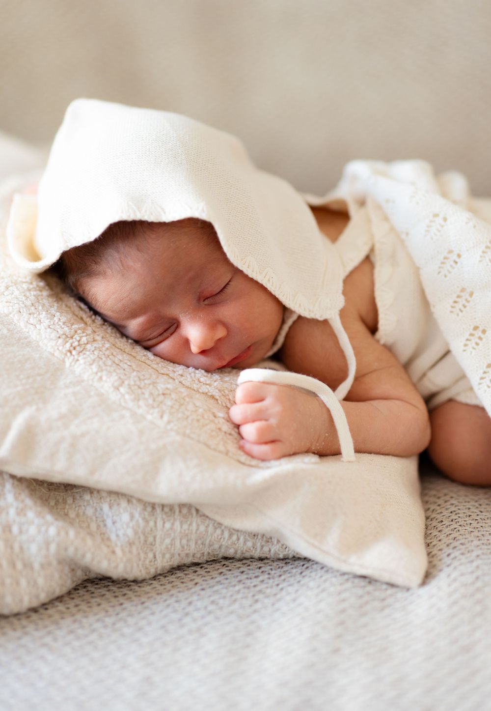 Sleeping newborn wrapped in soft white blanket on cream bedding.