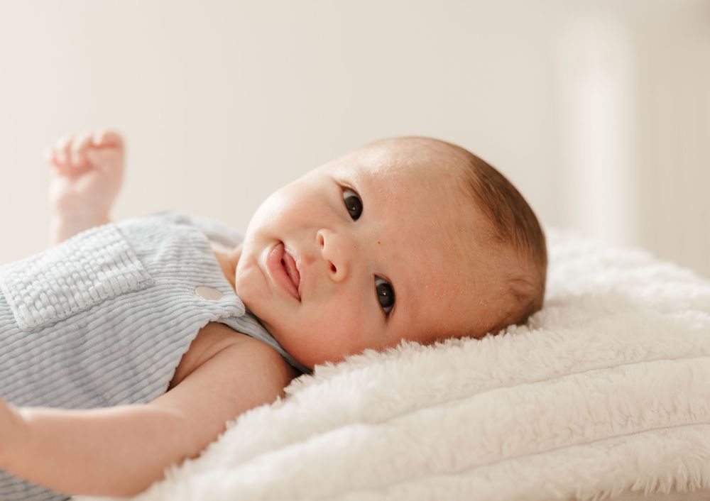 Baby in gray onesie lying on white plush blanket.