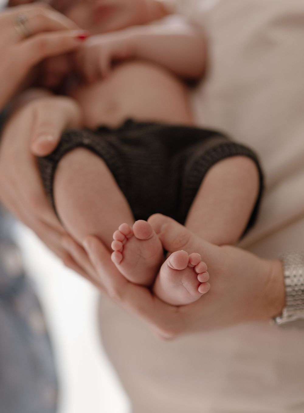 Close-up of tiny baby feet and hands being gently cradled.