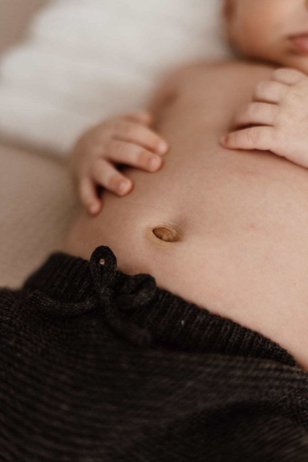Close-up of baby's belly and hands with black clothing detail.