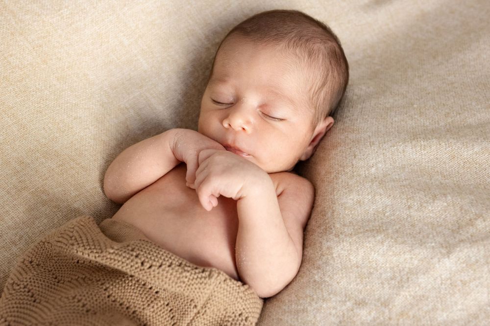 Peaceful sleeping newborn baby lying on beige fabric.