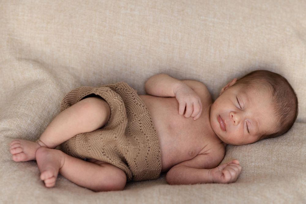 Sleeping newborn baby in brown wrap lying on textured linen.