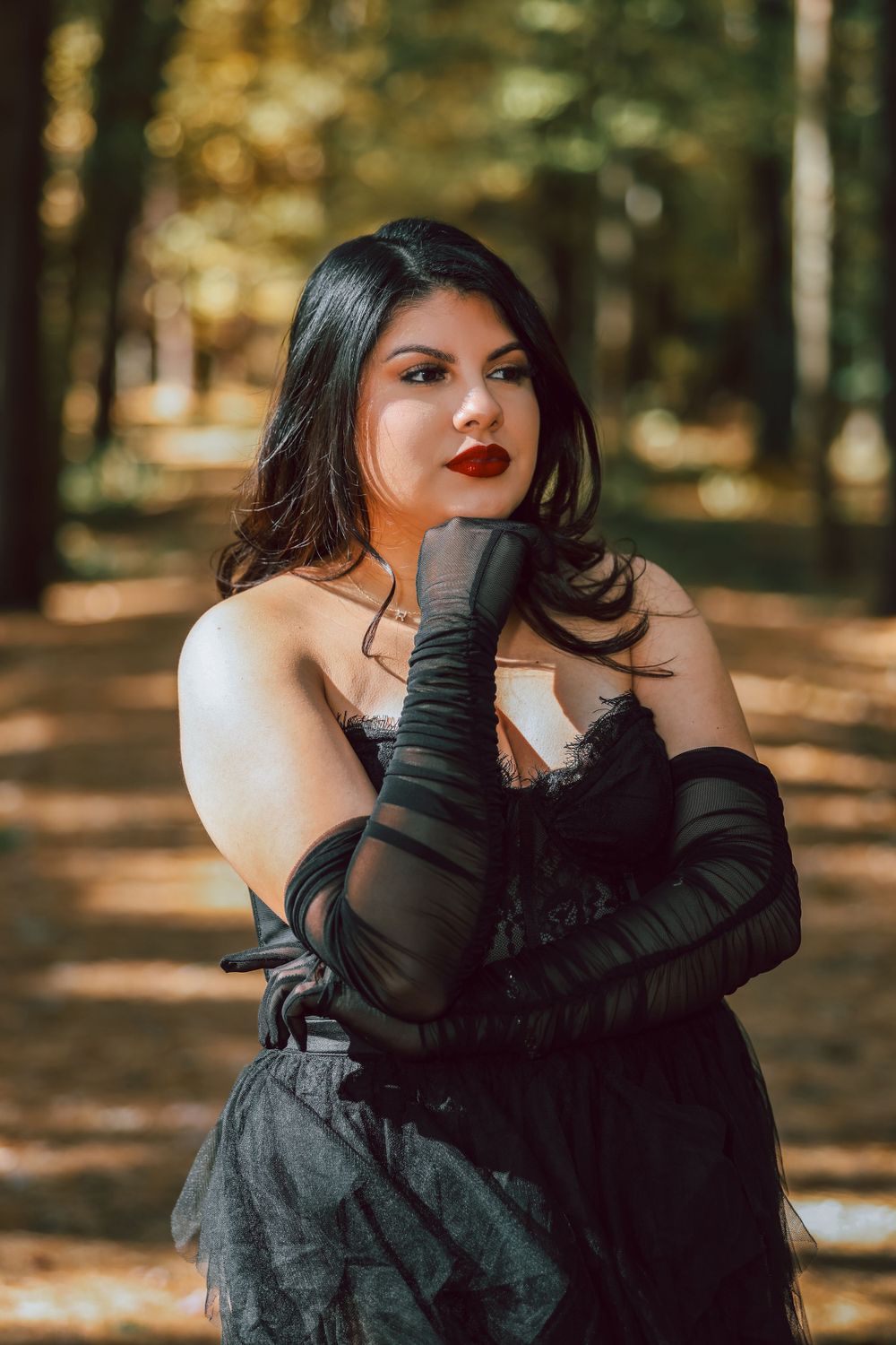 A glamorous portrait of a woman in black evening wear with long gloves in a forest setting.
