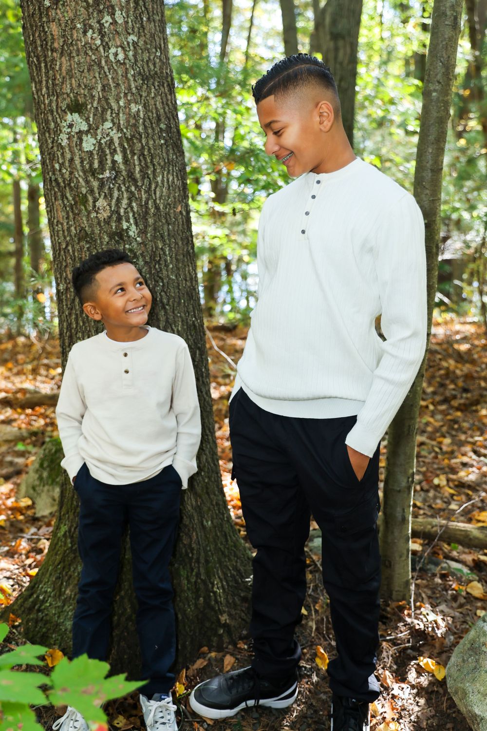 Two people wearing matching white sweaters standing next to a tree in an autumn forest.