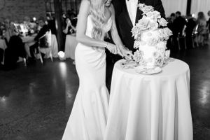 A couple cutting their elegant white wedding cake at their reception in black and white.