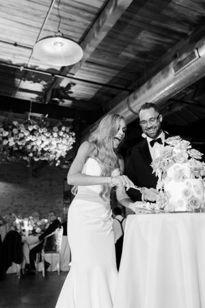 A candid moment of newlyweds laughing while cutting their wedding cake together.