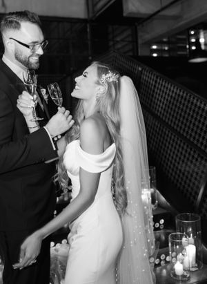 A romantic black and white photograph of a celebratory toast with candlelight in the background.