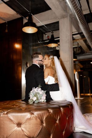 Romantic wedding couple shares intimate moment on leather ottoman in industrial venue.
