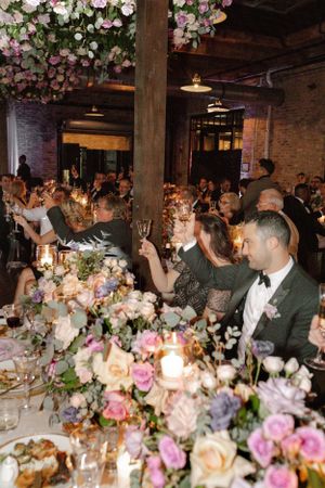 Wedding reception table adorned with pink and purple flowers under hanging floral installation.