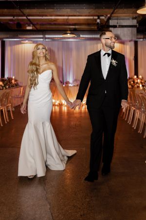 Couple walks hand in hand through industrial wedding venue with elegant decor.