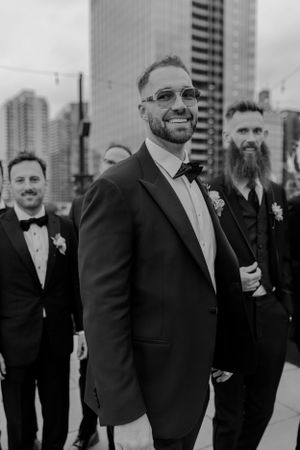 Groomsmen in classic tuxedos pose for black and white photo against city skyline.