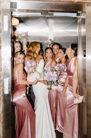 Bridal party in white and pink silk dresses squeeze into elevator for fun photo.